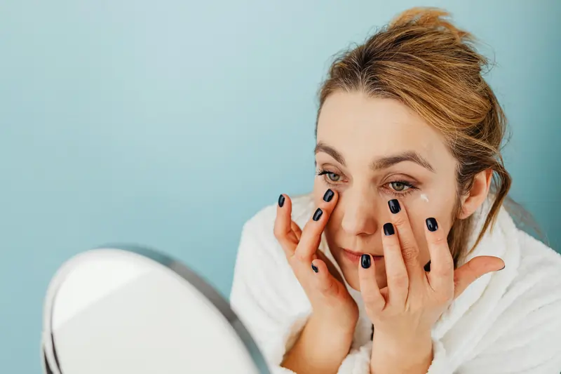 Donna si deterge e massaggia il viso con crema di fronte a uno specchio portatile | LaserMilano